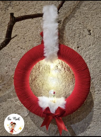 Couronne de Noël rouge avec une décoration blanche et des lumières intégrées.
