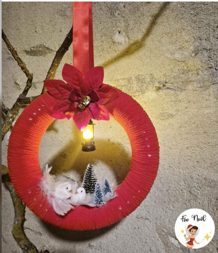 Couronne décorative rouge avec un flocon et des petits sapins, suspendue à un mur.